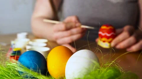 A young Woman Paints Easter Egg with a Brush on the background of Wooden Table Stock Footage 61743795