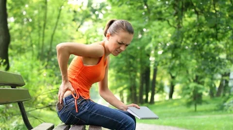 Young woman in the park with back pain, steadicam shot Stock Footage