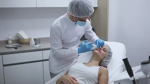 Young woman patient of beautician receiving rejuvenating facial injections Stock Footage