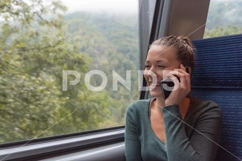 Young woman phoning with his smartphone during a journey in the train while s Stock Photos