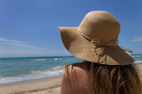 Young woman with picture hat sitting alone at the beach Stock Photos