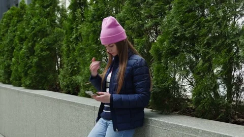 A young woman in a pink hat using smartphone by parapet and thujas. Stock Footage 273015331