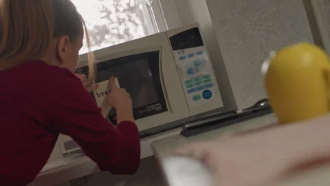 Young Woman Placing Bread Note on Microwave Door and Adjusting Oven Contents Stock Footage 344404557