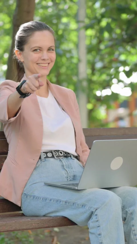 Young Woman Pointing at Camera while Using Laptop Outdoor Vidéo 319967449