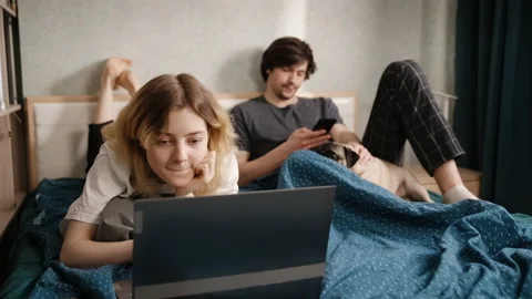 A young woman points at something to a guy on a laptop. The woman smiles. Stockbeeldmateriaal 197489244