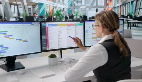 Young Woman Points At Task Board While Updating Project Schedule. Stock Photos