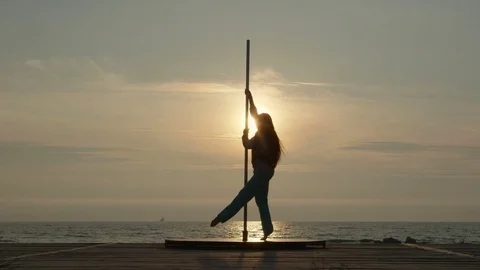 Young woman pole dancer stretching before outdoor poledance workout by the sea Stock Footage