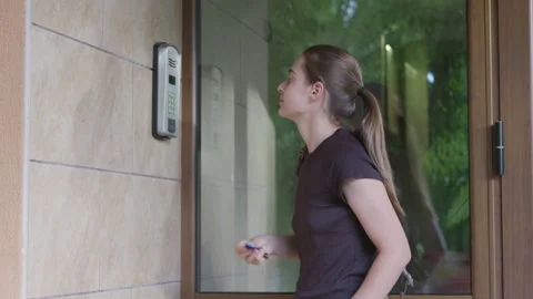 Young woman with ponytail approaches intercom system at entrance, preparing to Vidéo 340901784
