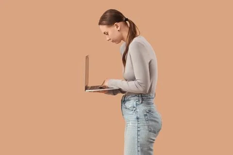 Young woman with poor posture using laptop on beige background Stock Photos