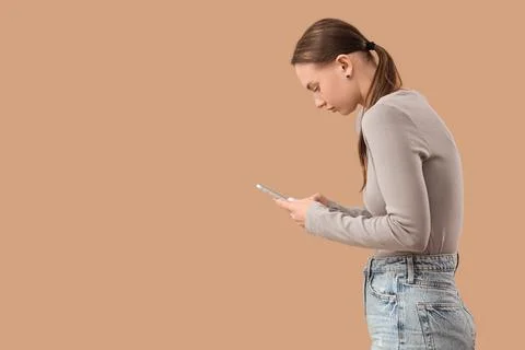 Young woman with poor posture using mobile phone on beige background Stock Photos