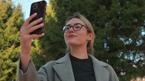 A young woman poses while taking selfies outdoors in bright sunlight. She Stock Footage 337642888
