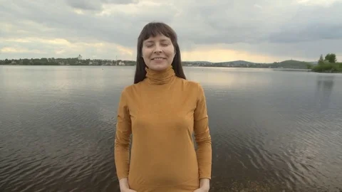 Young woman posing against the backdrop of a city pond on a cloudy day. Stock Footage 76631070