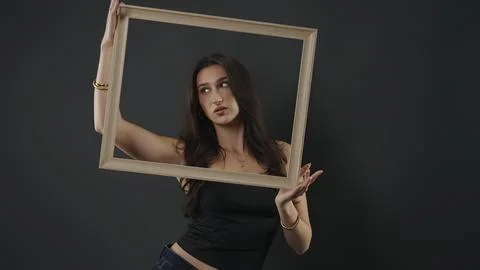 Young woman posing with empty frame in creative studio Stock Photos