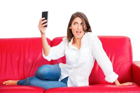 Young woman posing while taking selfie on sofa Stock Photos