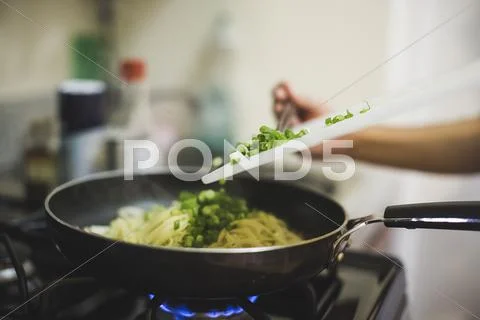 Young Woman Pouring Chopped Spring Onions Into Frying Pan