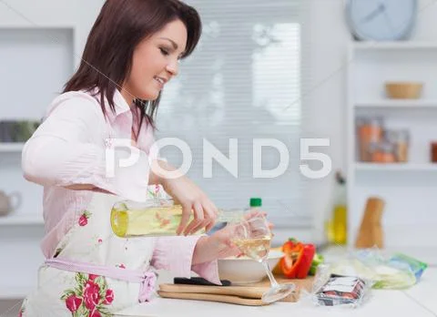 Young woman pouring wine while cooking food Stock Photos