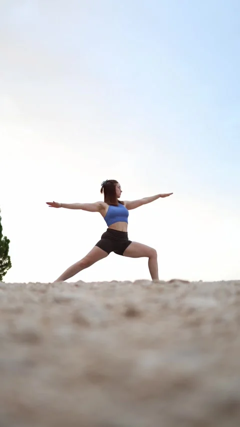 Young woman practices Warrior Two yoga pose on a beach Stock Footage 341318013