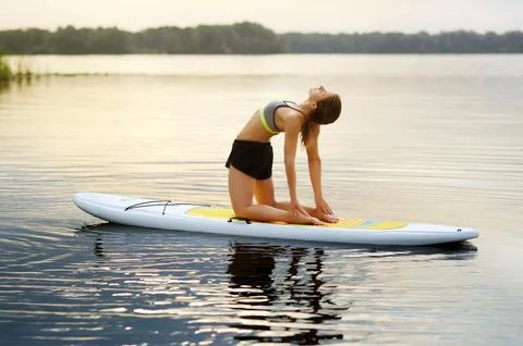 Young woman practicing  Camel yoga Pose on paddle board in the early morning Stock Photos