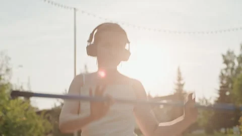 Young Woman Practicing Pole Vault in Park During Sunset with Headphones with Stock Footage 345848805