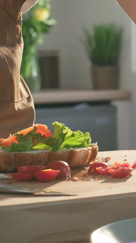 Young woman preparing breakfast puts lettuce salmon slices on croissant sandwich Stock Footage 309136681