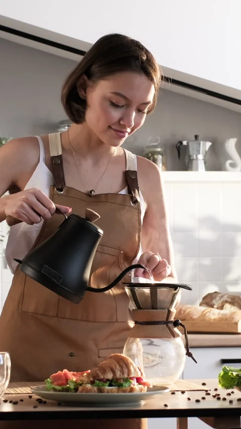 Young woman preparing drip coffee pouring water over paper filter in the kitchen Stock Footage 298319035