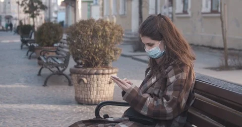 Young woman in protective mask using a mobile phone while sits on the bench Stock Footage 128264696