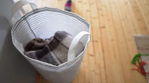 A young woman pulls a woolen knitted blanket from a laundry basket, on a wooden Stock Footage 114566791