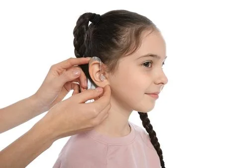 Young woman putting hearing aid in little girl's ear on white background Stock Photos