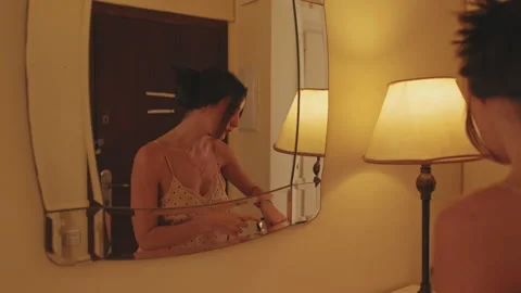 Young woman putting on makeup while standing in front of mirror Stock Footage 229509774