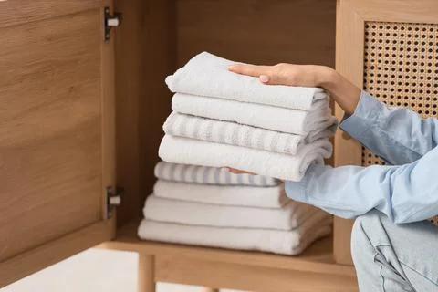 Young woman putting stack of clean towels into open drawer at home Stock Photos
