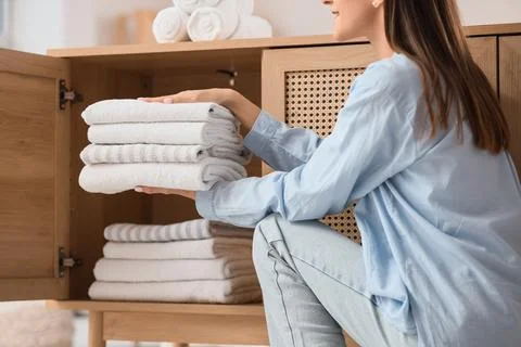 Young woman putting stack of clean towels into open drawer at home Stock Photos