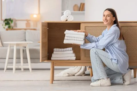 Young woman putting stack of clean towels into open drawer at home Stock Photos