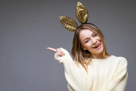 Young woman in rabbit ears shows tongue and finger to the side on background Stock Photos