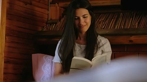 Young woman reading book in rustic wooden cabin interior, cozy lifestyle scene Stock Footage 336192992