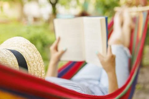 Young woman reading book while lying in comfortable hammock at green garden Stock Photos