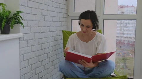 Young Woman Reading a Book by the Window on a Rainy Day Stock Footage 148366053