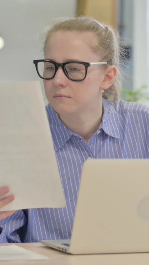 Young Woman Reading Document and Working on Laptop, vertical video Vídeos de archivo 328550178