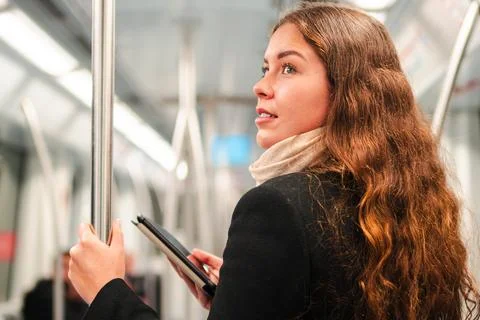 Young woman reading an e-reader while standing in a subway train, showcasin.. Stock Photos
