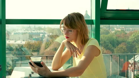 Young woman reading something on e-book sitting in cafe, 4K Stock Footage 107420565