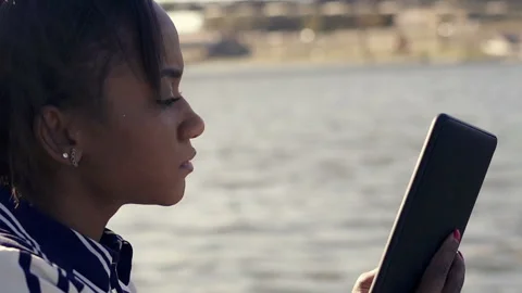 Young woman reading something on e-book sitting close to the river, slow motion Stock Footage 135826486