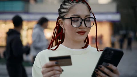 Young woman with red dreadlocks making mobile payment outdoors in city Stock Footage 340761332