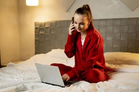 Young Woman in Red Pajamas Using Laptop and Smartphone in Bedroom at Night 스톡 사진