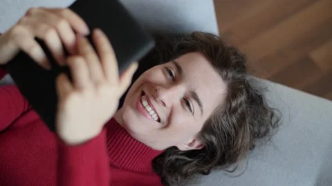 Young woman with red pullover reading e-book on grey couch at home. Stock Footage 142844201