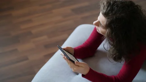 Young woman with red pullover reading e-book on grey couch at home. Stock Footage 142844237