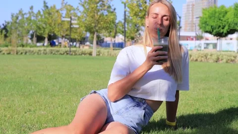 Young woman relaxing on grass drinking iced matcha latte with straw on summer Stock Footage 315744375