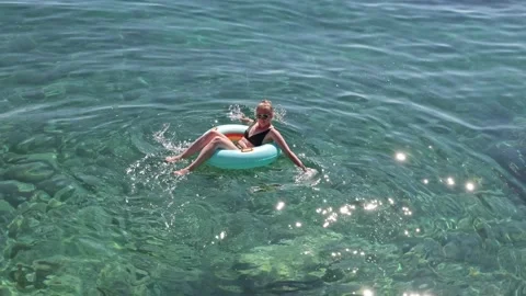 Young woman relaxing on inflatable float in clear turquoise water, enjoying a Stock Footage 313756898