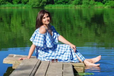 Young woman resting on a wooden bridge and wets feet in the river. Stock Photos
