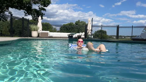 Young woman rests on pool float alone in the middle of ritzy affluent home pool Video stock 231177109
