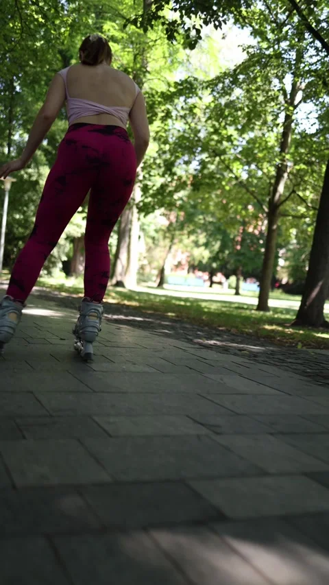 Young woman roller skating through a green park viewed from behind Video stock 341476554