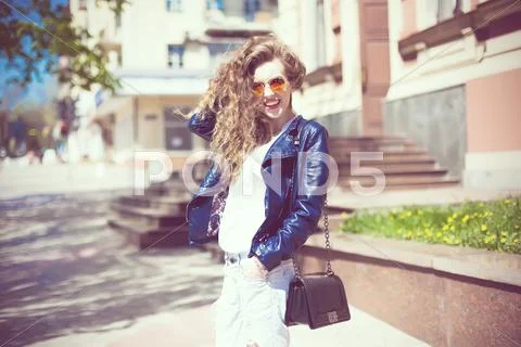 Young woman in round hipster sunglasses and leather jacket with long curly ha Stock Photos